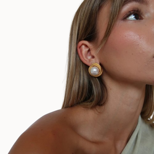 Close-up of a person wearing a gold earring with a pearl on a white background