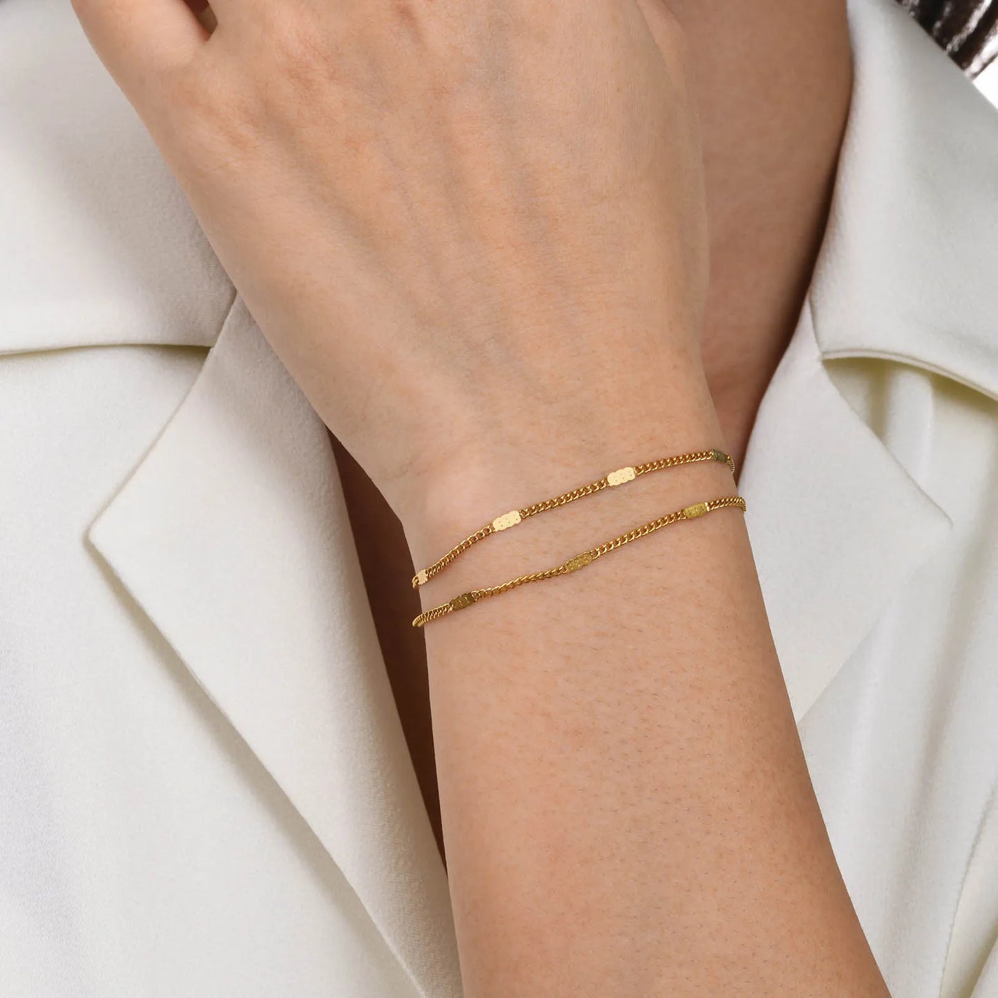 Gold bracelets on a person's wrist with a white background