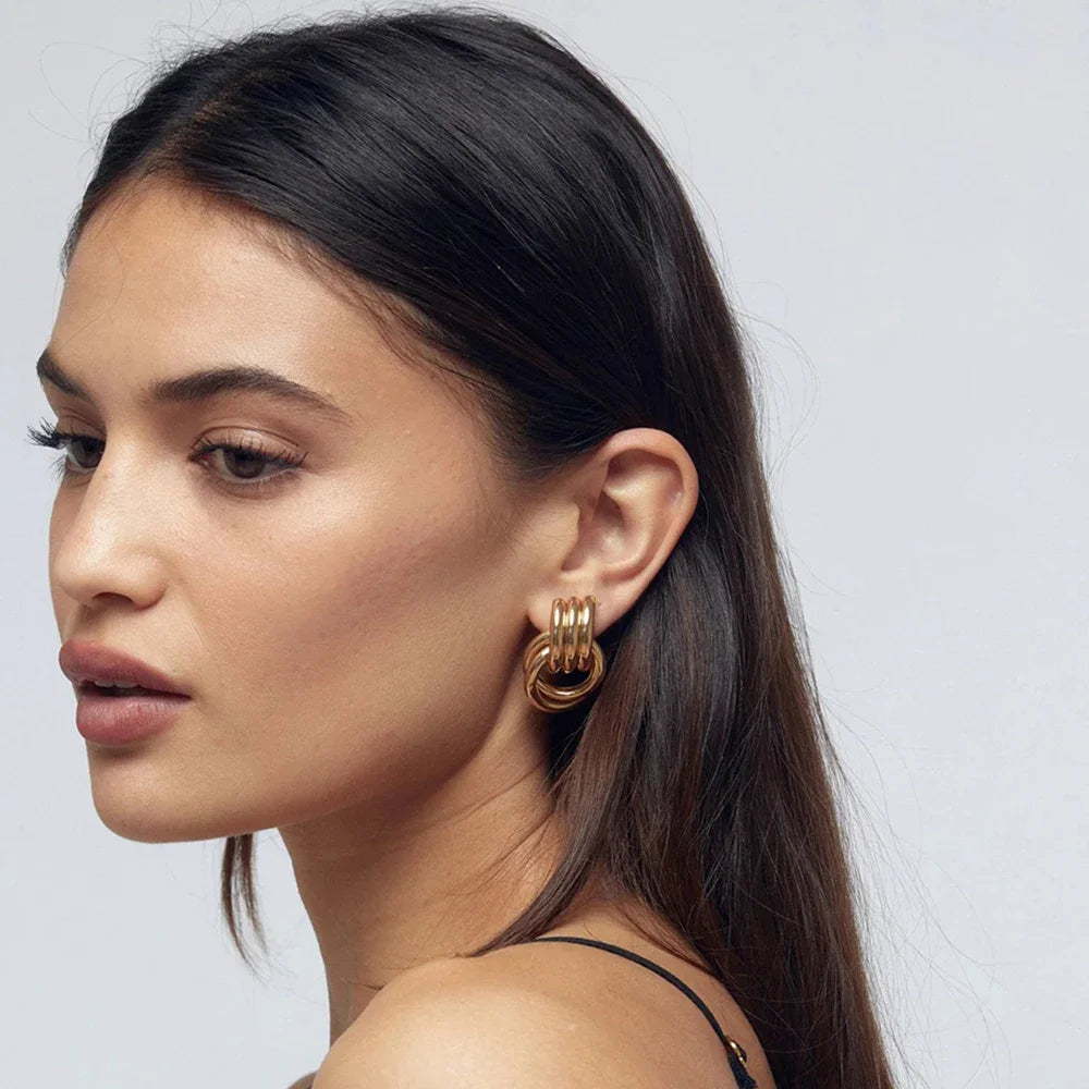 Close-up of a woman wearing gold hoop earrings against a plain background