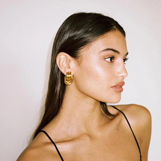 Woman wearing gold hoop earrings against a plain background