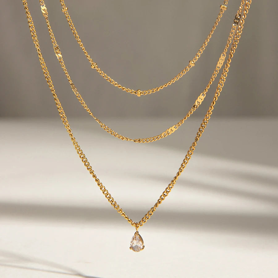 Gold necklace with a teardrop pendant on a neutral background