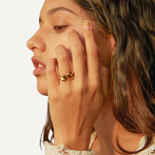 Close-up of a woman wearing a gold ring on her finger against a neutral background