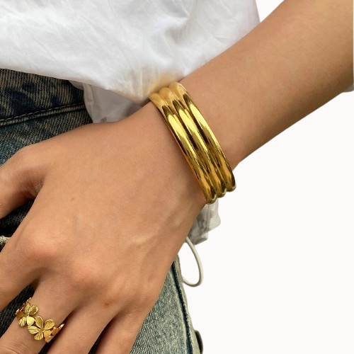 Gold bracelet and ring on a wrist with a white background