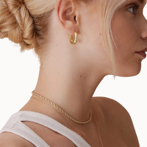 Close-up of a woman wearing gold hoop earrings and a delicate gold necklace on a white background