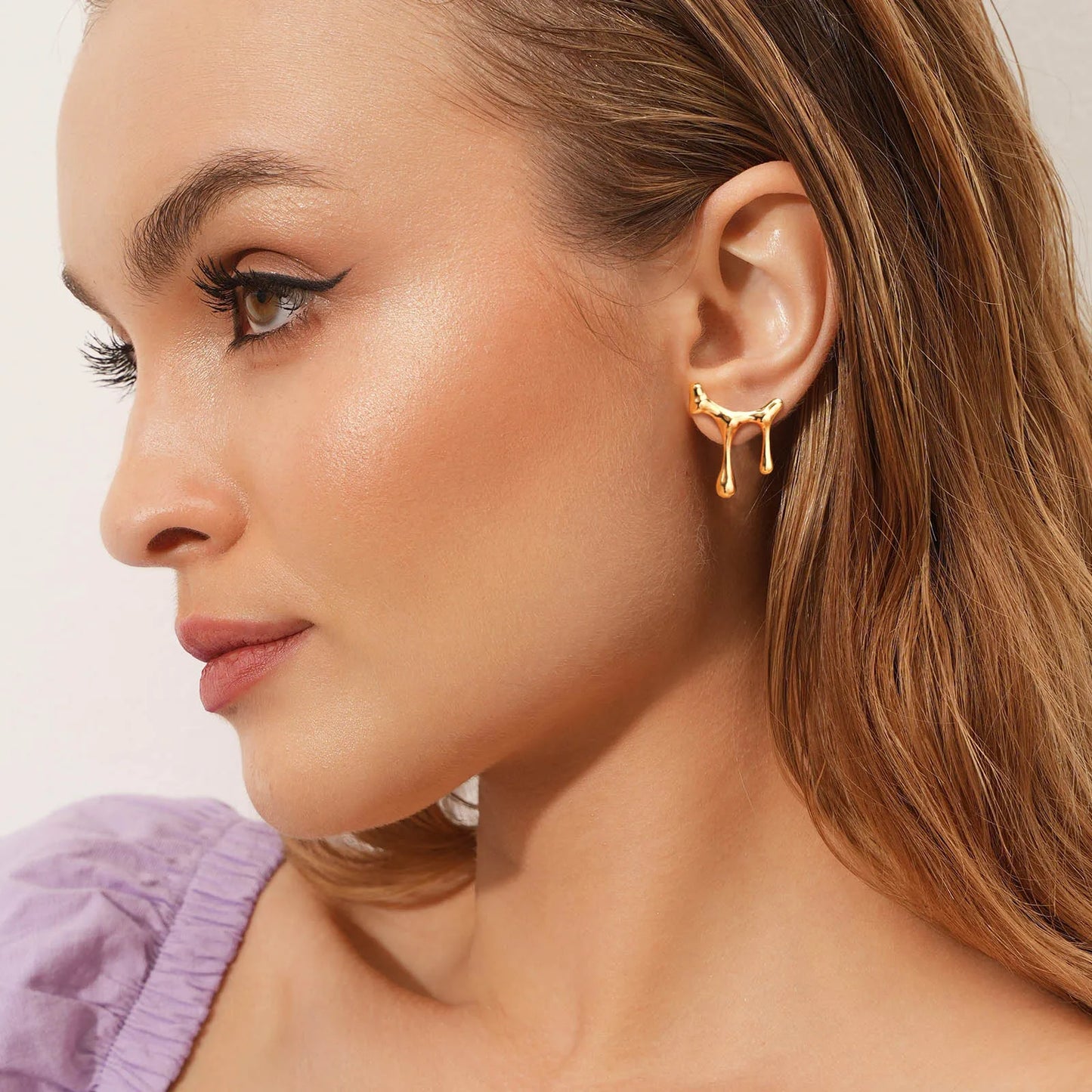 Close-up of a woman wearing a gold earring with a light background