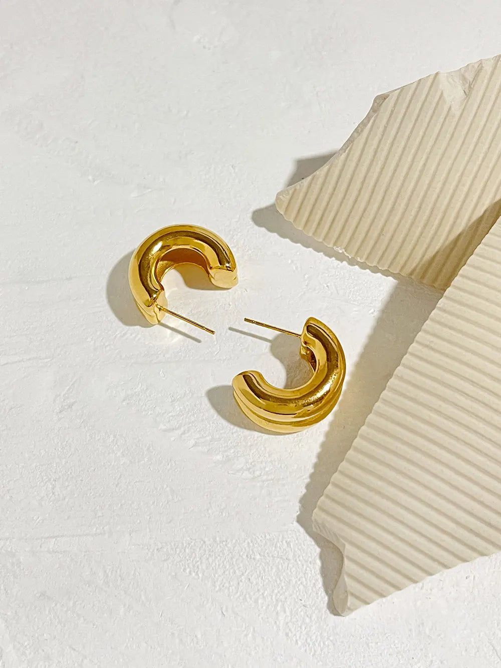 Gold hoop earrings on a textured white surface with a beige paper strip.
