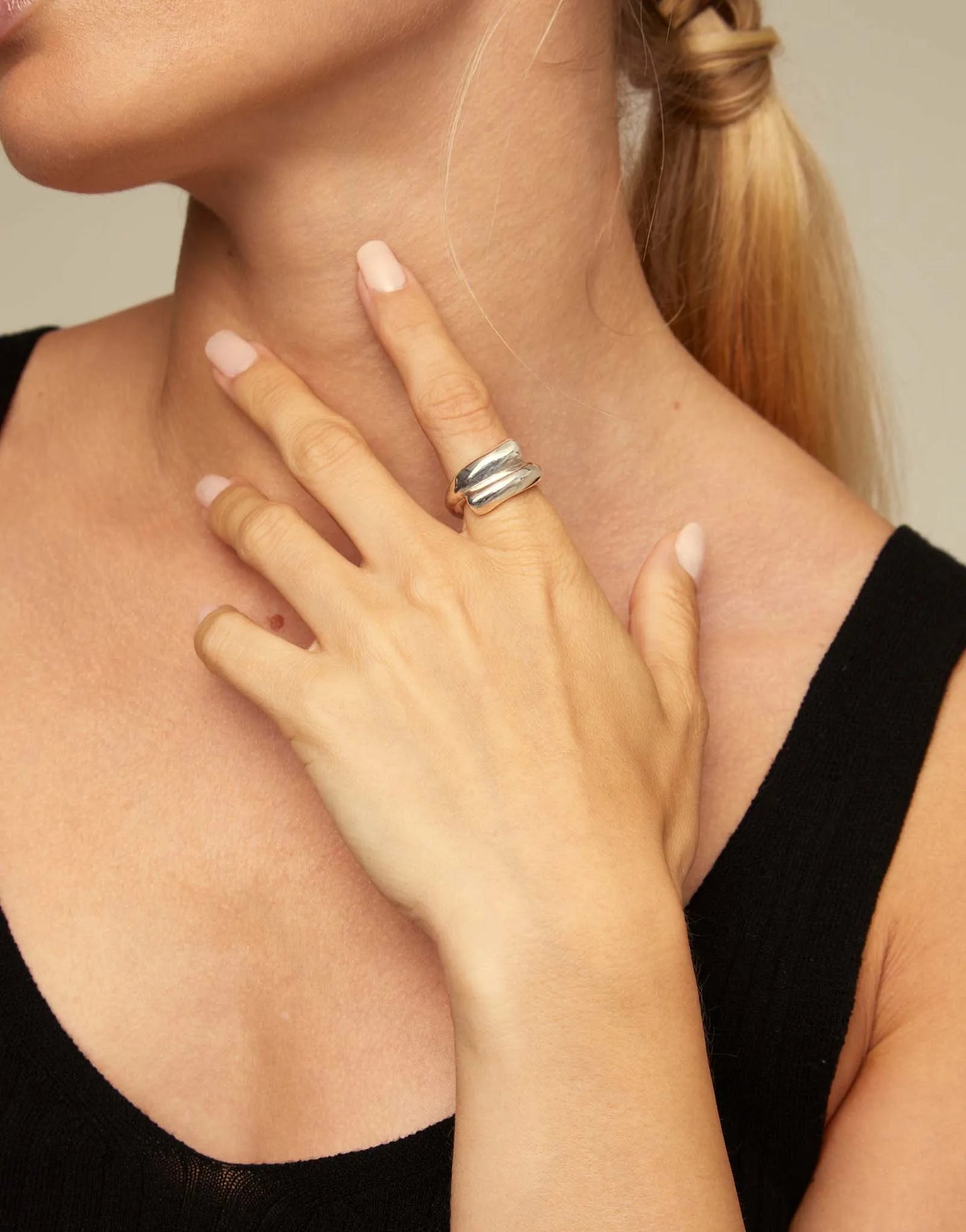 Close-up of a woman wearing a silver ring on her hand touching her neck.