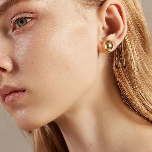 Close-up of a woman wearing gold stud earrings with a neutral background
