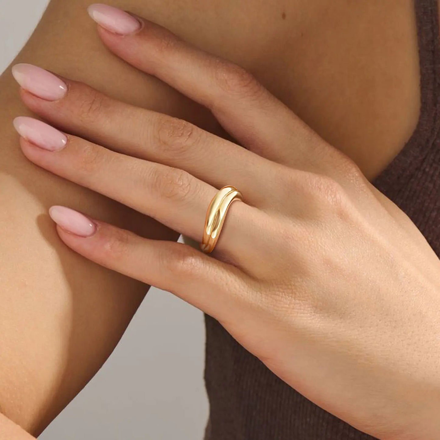 Hand wearing a gold ring with a neutral background