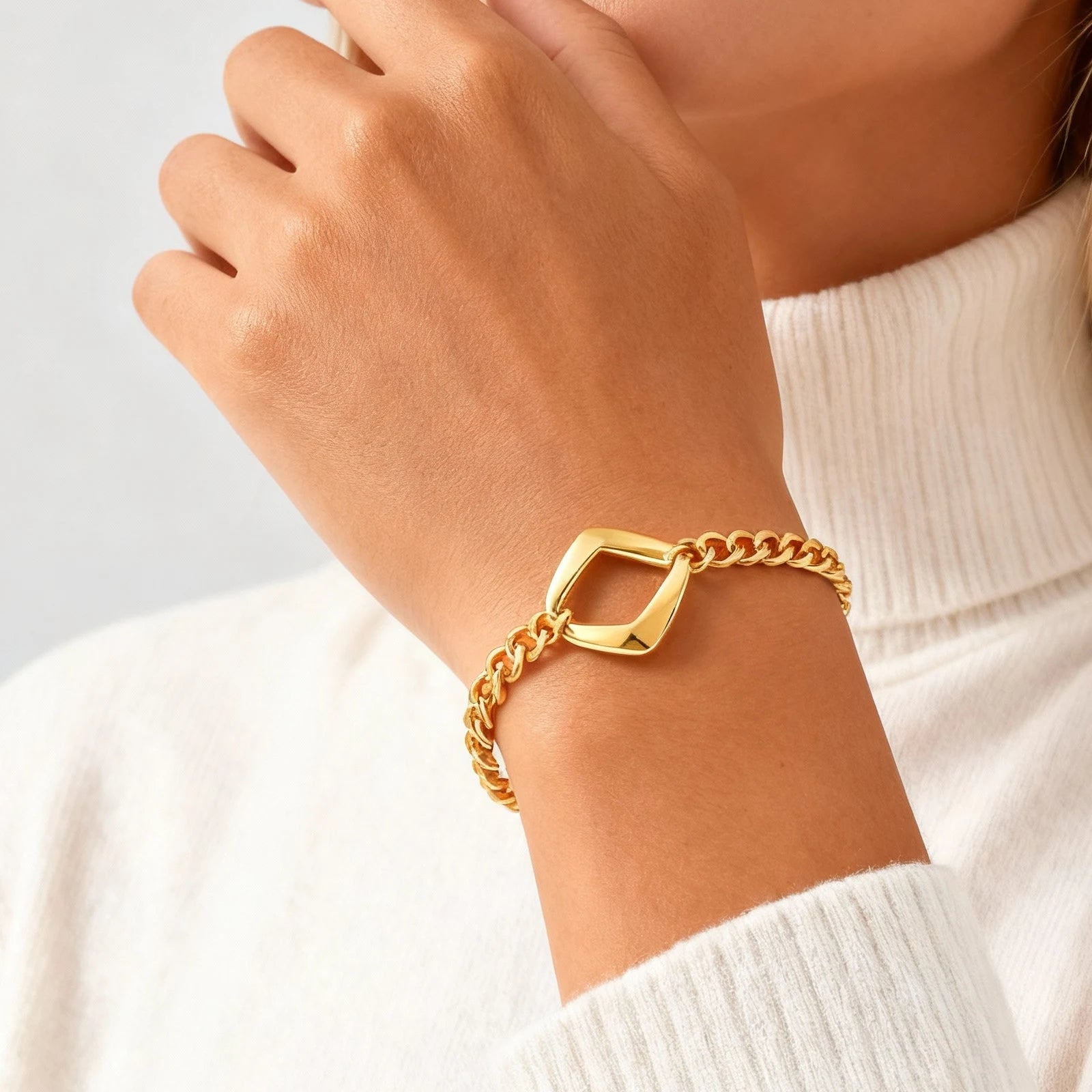 Gold chain bracelet on a wrist with a neutral background