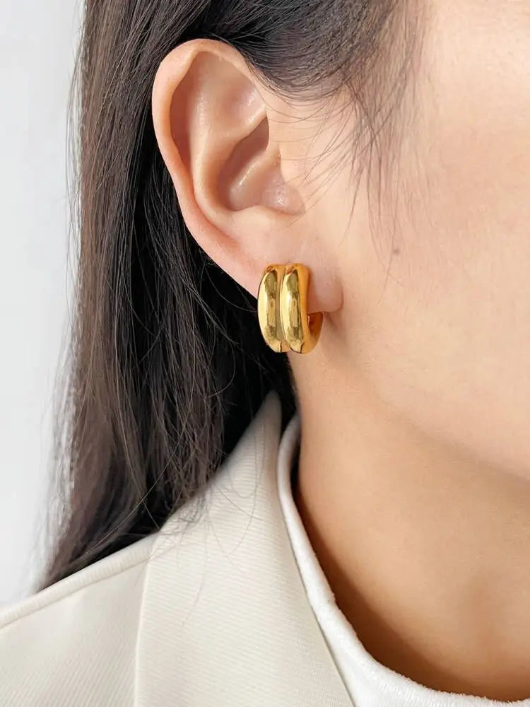 Gold hoop earrings worn by a person with a neutral background