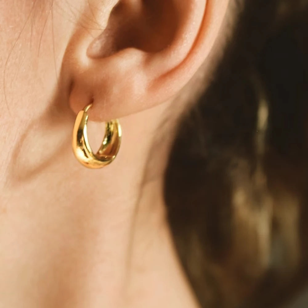 Gold hoop earring worn on an ear with a blurred background