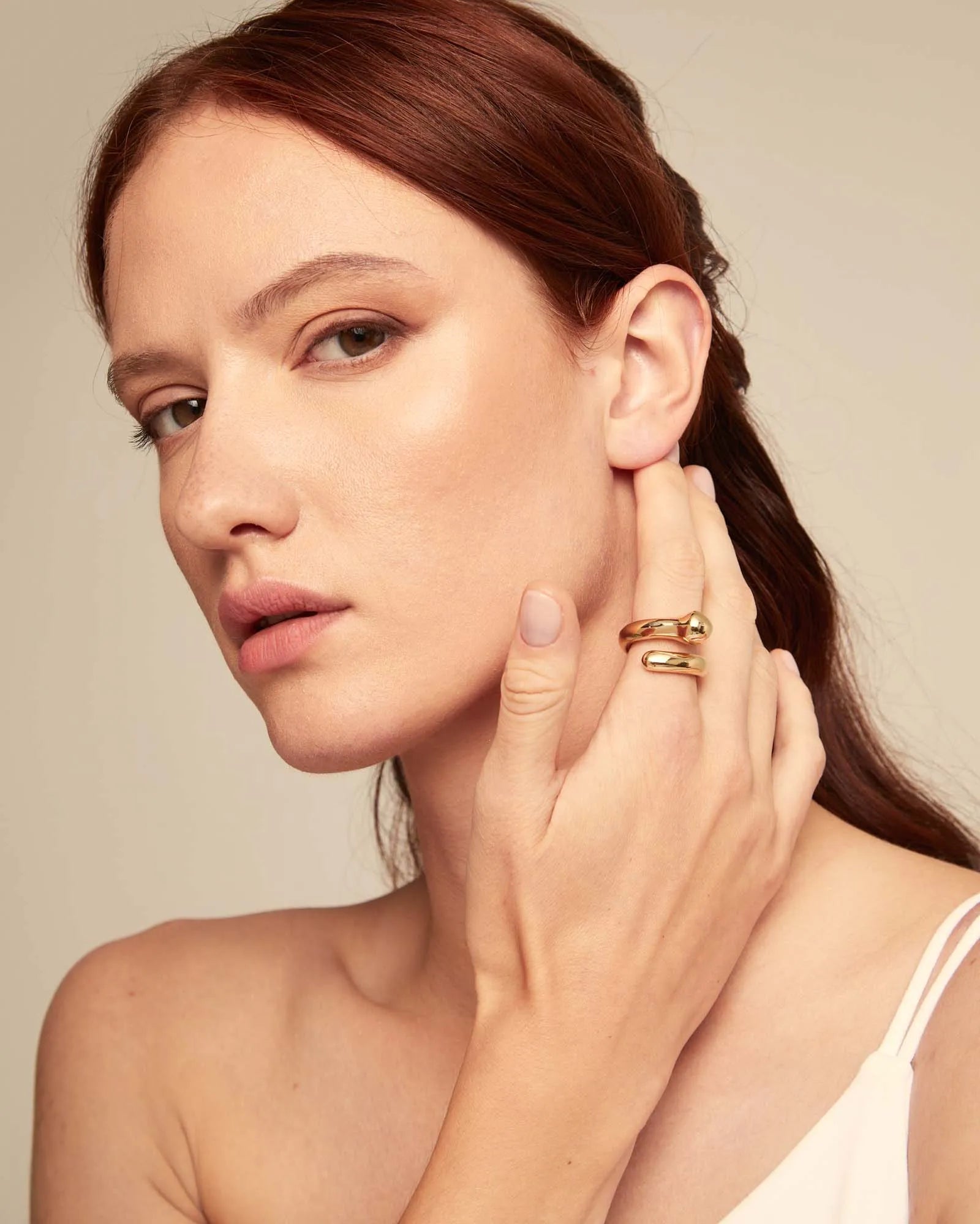Woman wearing gold rings on a beige background