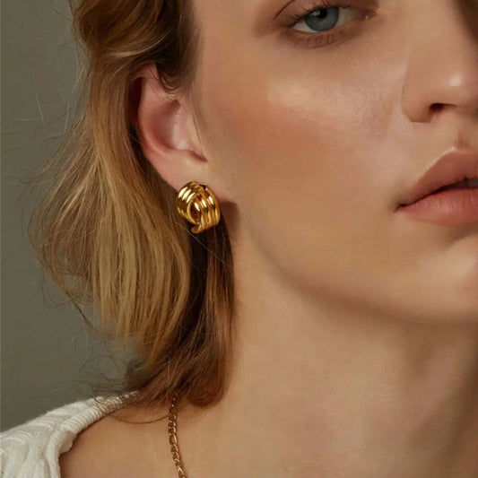 Close-up of a woman wearing gold hoop earrings with a neutral background