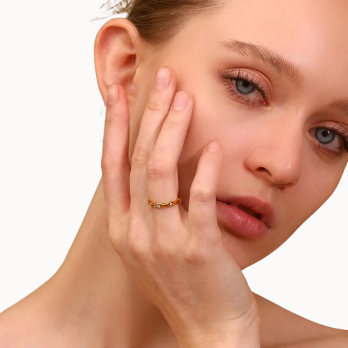 Woman with hand on face wearing a gold ring against a white background