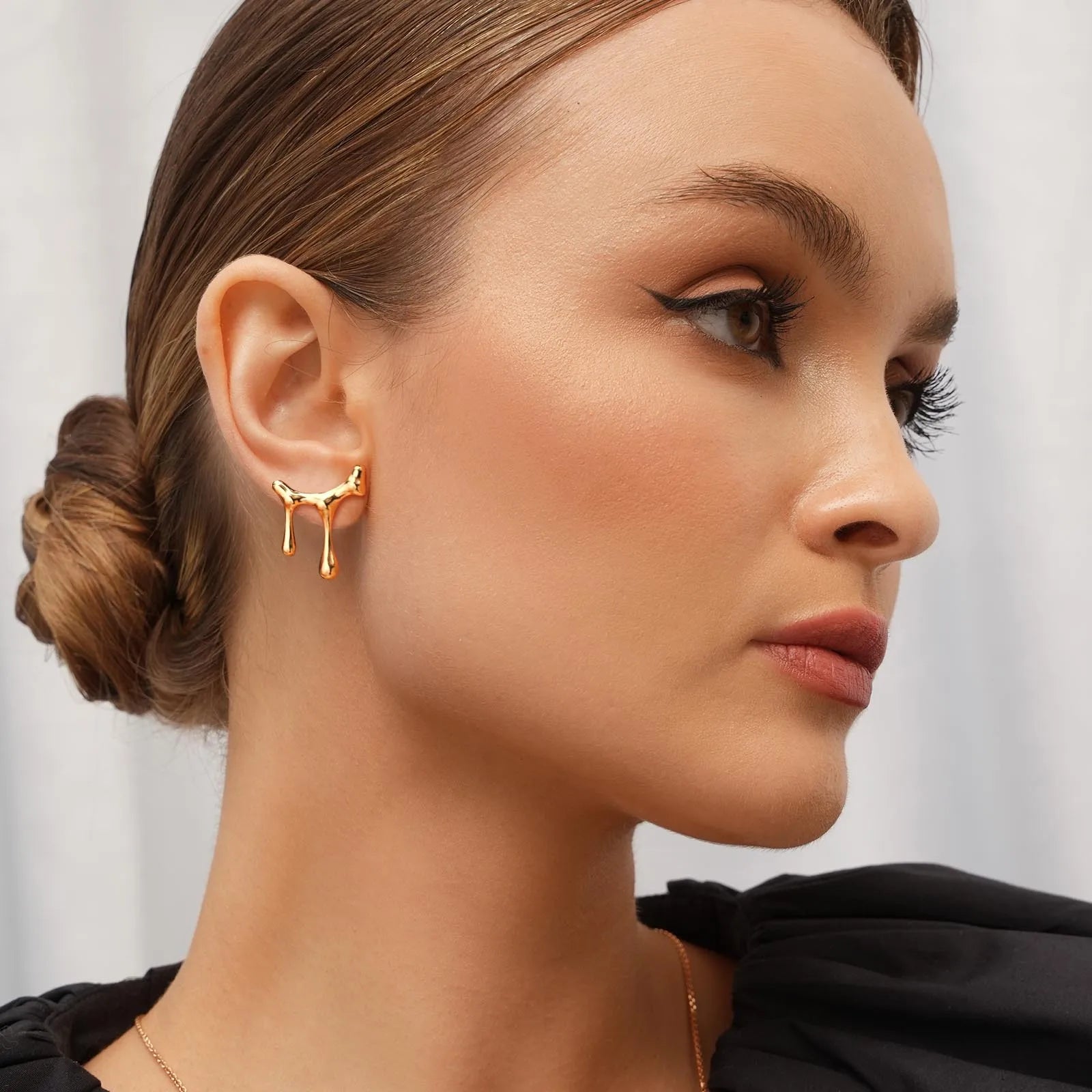 Close-up of a woman wearing gold earrings with a neutral background