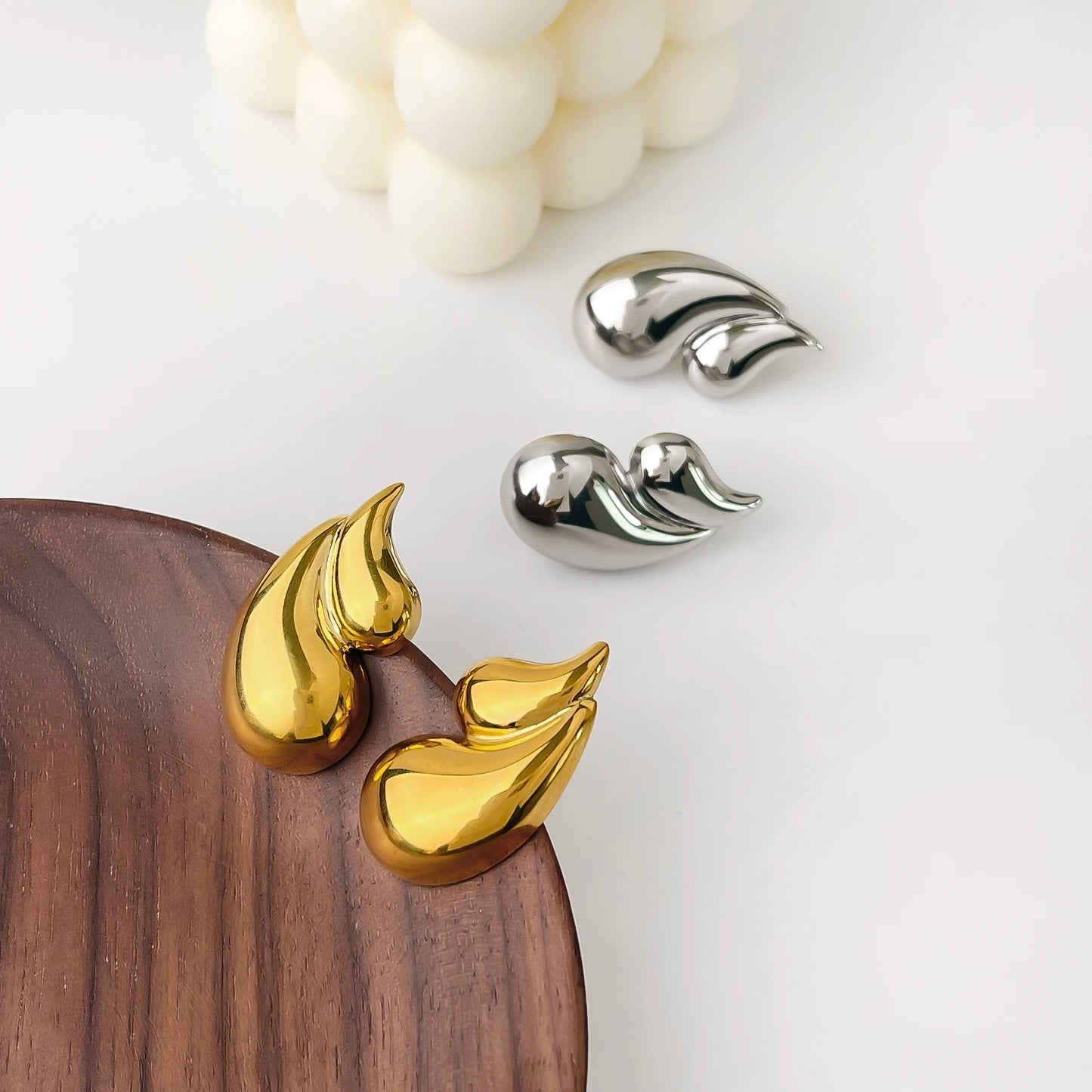 Gold and silver leaf-shaped earrings on a wooden surface with a white background