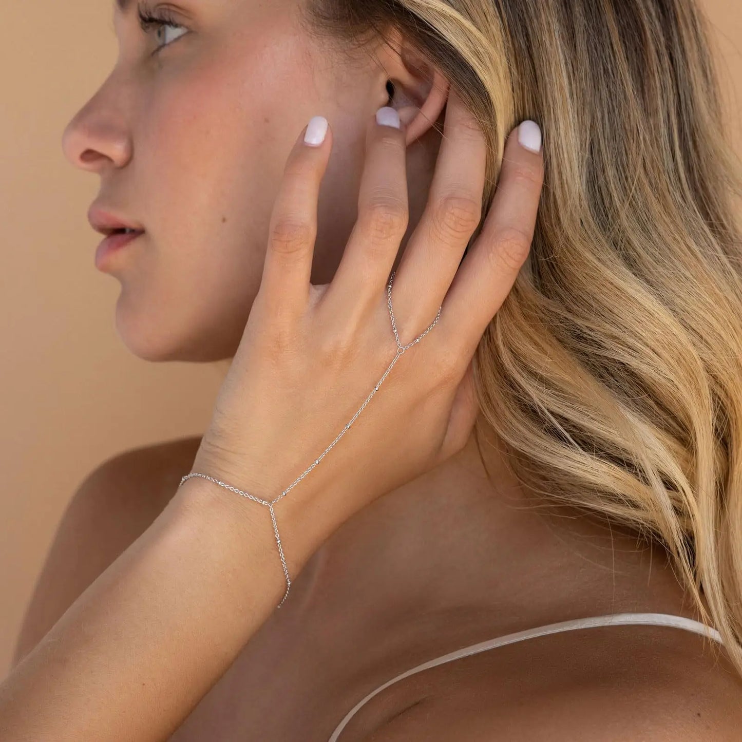 Woman wearing a delicate silver bracelet on her wrist with a neutral background