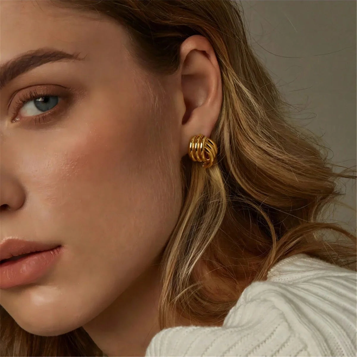 Close-up of a woman wearing gold hoop earrings with a neutral background