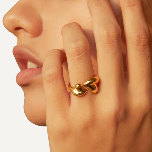 Close-up of a hand wearing a gold ring with leaf designs on a neutral background